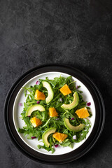 Salad with avocado, orange, ruccola and red onion on black stone background.  Vertical orientation.  Flat lay. Copy space. 