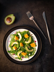 Salad with avocado, orange, ruccola and red onion on black stone background.  Vertical orientation.  Flat lay.