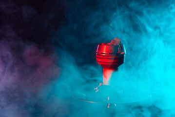 red hot shisha coals in a metal hookah bowl against a background of multicolored smoke