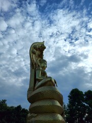 Golden Buddha statue on a pedestal, background of trees and sky.