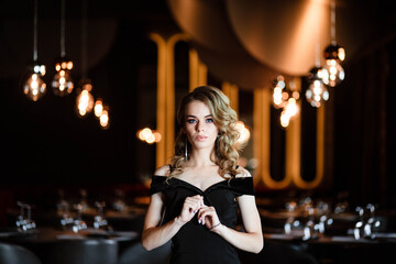 Plakat Beautiful blonde, young girl. Portrait of a young girl in a restaurant. Young girl in a restaurant on a black background. Portrait of a girl in a black dress. Young girl.