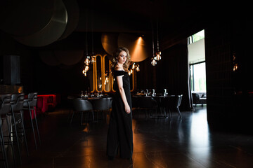 Beautiful blonde, young girl. Portrait of a young girl in a restaurant. Young girl in a restaurant on a black background. Portrait of a girl in a black dress. Young girl.