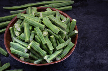 Cut green moringa drumstics in wooden bowl, black backround, copy space