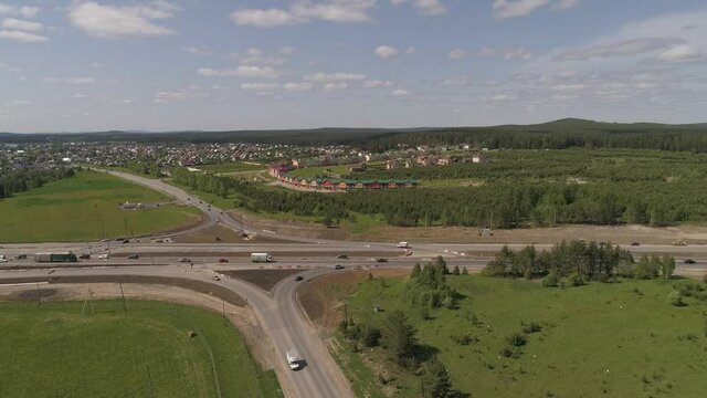 02. Aerial view of construction of a highway section and bridge. Cars are going from both sides. The scheme of transport movement has changed. Near the road field, forest and village. A sunny summer d
