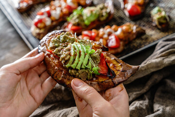 Hand hold baked sweet potato toasts with roasted chickpeas, tomatoes, goat cheese, avocado,...