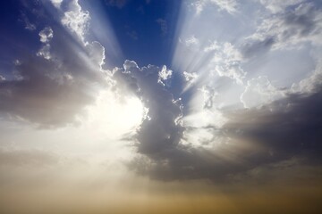 Bright sun rays pierce white clouds. Scenic sunny cloud scape. Blinding sun shines through the clouds. High contrast photography. Divine sky. Picturesque sky scape.