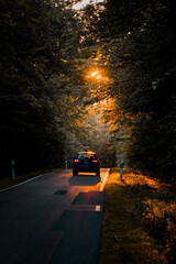 A car driving inthe middle of a dark forest with bright colorful sunset spotlight and illuminated natural scene. Driving in the summer evening on a beautiful road. Harz Mountains, Harz National Park 