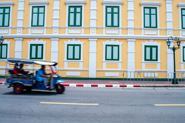 tuk-tuk on the road in bangkok with yellow building background, speed motion.Moving Tuk tuk taxi with windows wall of The Ministry of Defence in Bangkok, Thailand