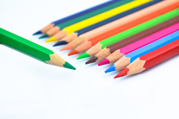 Line of different colored wood pencil crayons pointing at a green color pencil