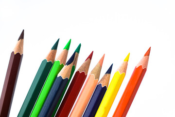 Nine different colored wood pencil crayons scattered on a white background