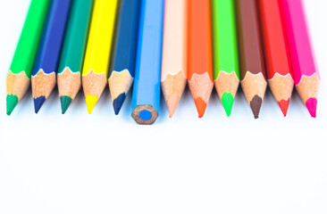 One line of different colored wood pencil crayons placed on a white paper background