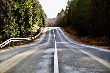 Straight empty asphalt road through the coniferous forest. Modern countryside road leading into the distance. Highway surface close up. Diminishing perspective road view. Traveling by car. Road trip.