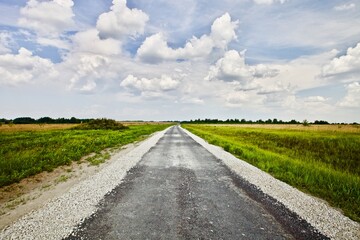 Countryside road leading through the fields. Countryside road on sunny summer day. Old empty asphalt road in the countryside. Road leading to the horizon. Traveling by car. Adventure and freedom.