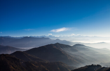 Naklejka na ściany i meble Sunrise. Early morning in Himalaya mountains. Mist-shrouded mountain peaks. Bright blinding sun. Blue sky. Fog. Mountains landscape. Highlands nature. Backgrounds. Nepal.