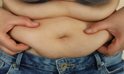 Fototapeta premium A Caucasian woman holds extra fat on her stomach with her hands. Selective focus. Obesity. Excess weight.