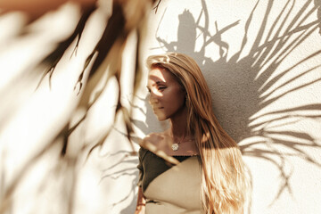 Beautiful tanned blonde woman in dark green top smiles and poses outside. Attractive long-haired...