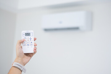 hand using remote controller for adjust Air conditioner inside the room at home