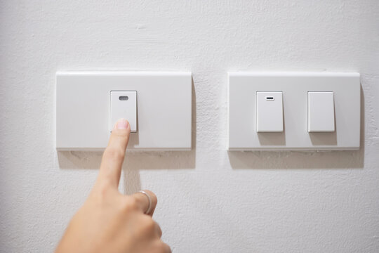 Female finger is turn on or off on light switch on white wall at home. Energy Saving, power, electrical and lifestyle concepts .