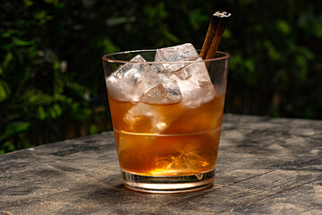 old fashioned cocktail in short glass on table with cinnamon garnish on green background 
