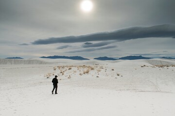 Figure in black walking along dunes in White Sands National Park in New Mexico with sun and grey skies 