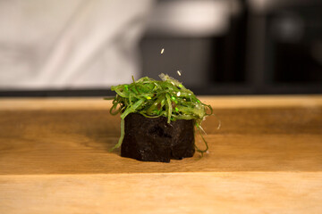 Japanese traditional Gunkan Maki Roll with Hiyashi Wakame seaweed and sesames. Just cooked Pan Asian dish on wooden board. Rice and Chukka wrapped in nori. Chef on background. Flying sesame seeds
