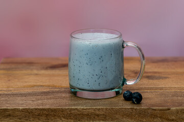 Glass with purple blueberry smoothie on wooden table against pink background