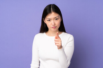 Young asian woman isolated on purple background frustrated and pointing to the front