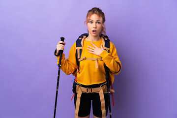 Teenager girl with backpack and trekking poles over isolated purple background surprised and shocked while looking right