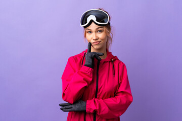 Skier teenager girl with snowboarding glasses over isolated purple background and thinking