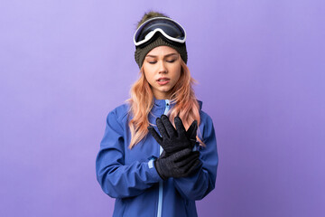 Skier teenager girl with snowboarding glasses over isolated purple background suffering from pain in hands