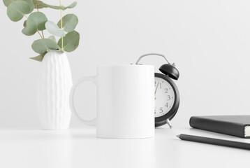 White mug mockup with eucalyptus in a vase and workspace accessories on a white table.