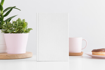 White book mockup with succulent plants in  pots, clock and workspace accessories on a white table.