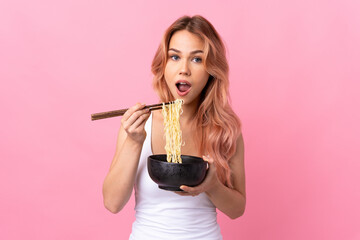 Teenager girl over isolated pink background holding a bowl of noodles with chopsticks and eating it