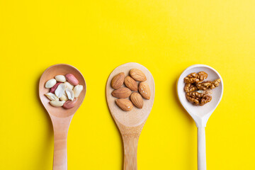nuts in wooden spoon on yellow, flat lay and place for text