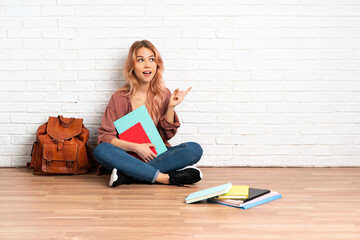 Teenager student woman with pink hair sitting on the floor at indoors intending to realizes the solution while lifting a finger up