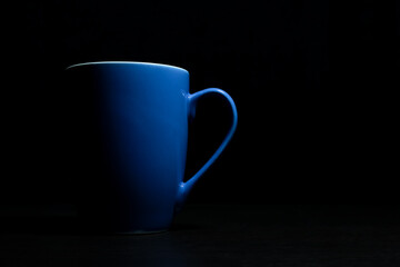 Low light view and copy space. Blue ceramic cup some light hits the surface placed on the dark shadows.