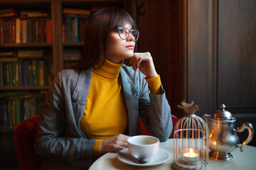 Beautiful dreamy girl in stylish sharp glasses. With a cup in his hands.