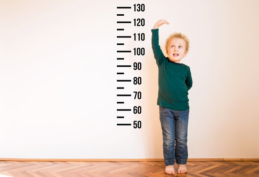 Little boy measuring height near white wall. Copy space