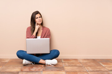 Teenager student girl sitting on the floor with a laptop having doubts