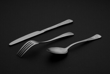 Kitchen cutlery placed on black background. Scene consists of knife, fork and a spoon