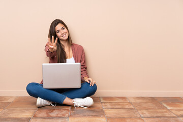 Teenager student girl sitting on the floor with a laptop happy and counting four with fingers