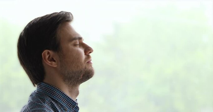 Peaceful man pose aside near window background closed eyes breath fresh air feels calm. Anxiety relief, brings internal state in order exercise, close up side view face. No stress, mindfulness concept