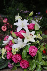 Gesteck mit weißen Lilien und pinken Rosen schmückt ein Grab nach Beerdigung