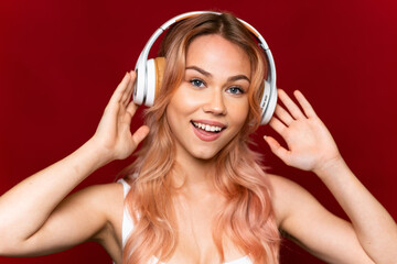 Fototapeta premium Teenager girl with pink hair listening music over isolated red background