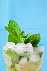 Cocktail mojito with mint leaves, lime and ice on a blue background.