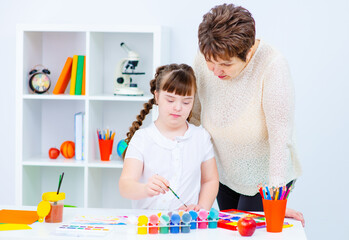 Teacher helps a child with down syndrome draw while holding a brush