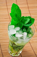 Cocktail mojito with mint leaves, lime and ice on a bamboo background.