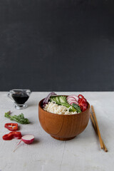 Noodles and vegetables in a wooden bowl stand on the table, next to beautifully sliced vegetables, chopsticks, soy sauce. Thai and asian sharp food, beautiful serve. Light photo, minimalism.