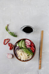 Noodles and vegetables in a wooden bowl stand on the table, next to beautifully sliced vegetables, chopsticks, soy sauce. Thai and asian sharp food, beautiful serve. Light photo, minimalism.