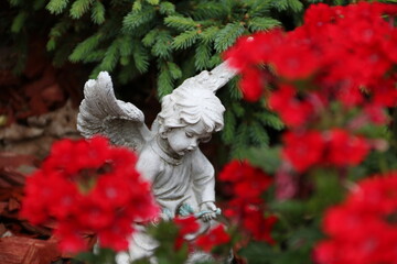 Friedhofsengel zwischen roten Blumen auf einem Grab